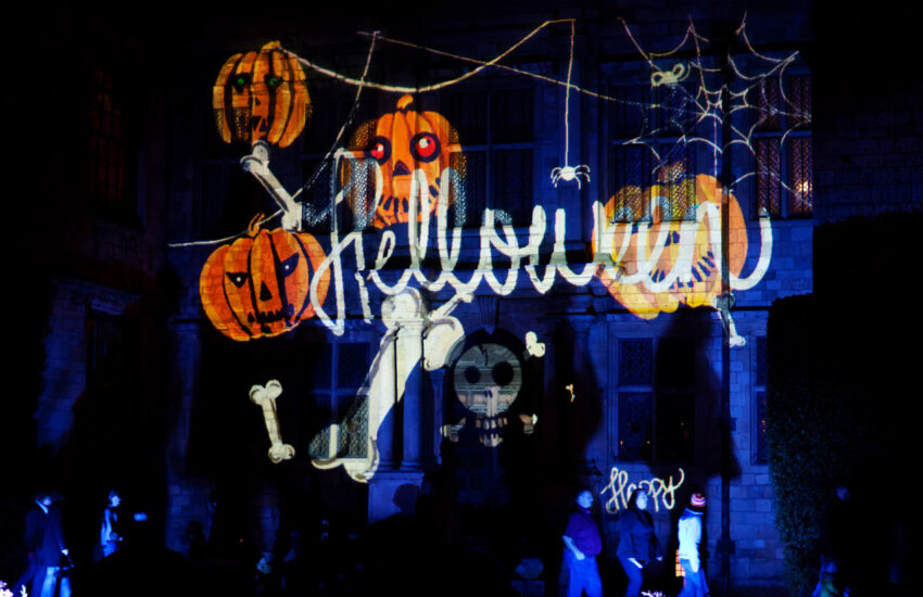 Spooky house lit by projector that highlights jack-o-lanterns and Halloween typed out